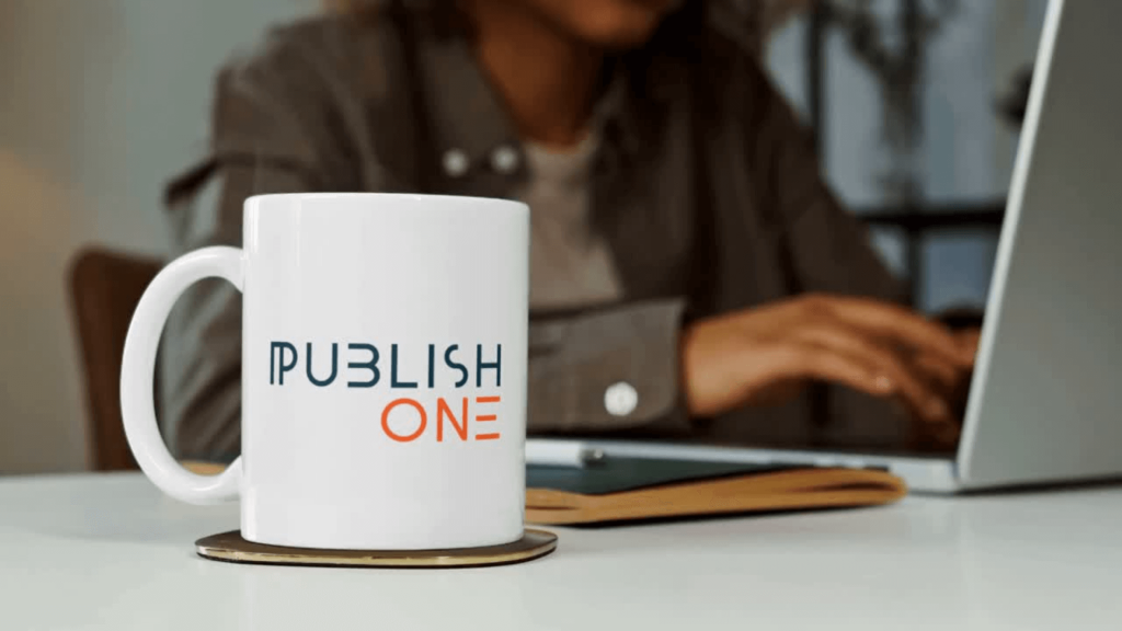 A person behind a laptop drinking from a PublishOne cup